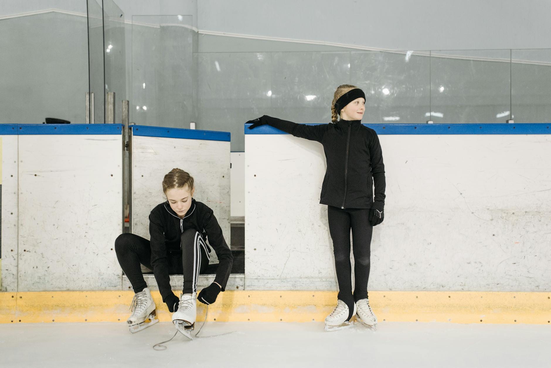 Dwie dziewczynki zakładają łyżwy na trening na krytym lodowisku
