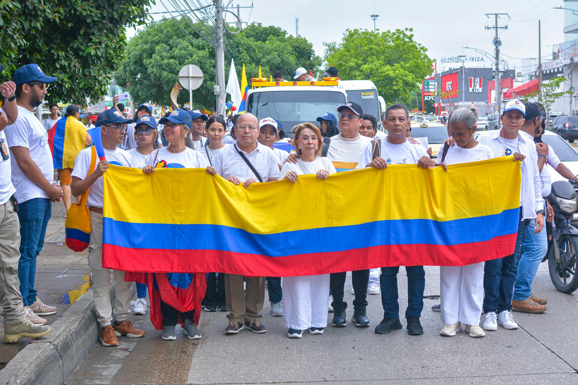 Grupa ludzi na ulicznej paradzie macha dużą flagą Kolumbii