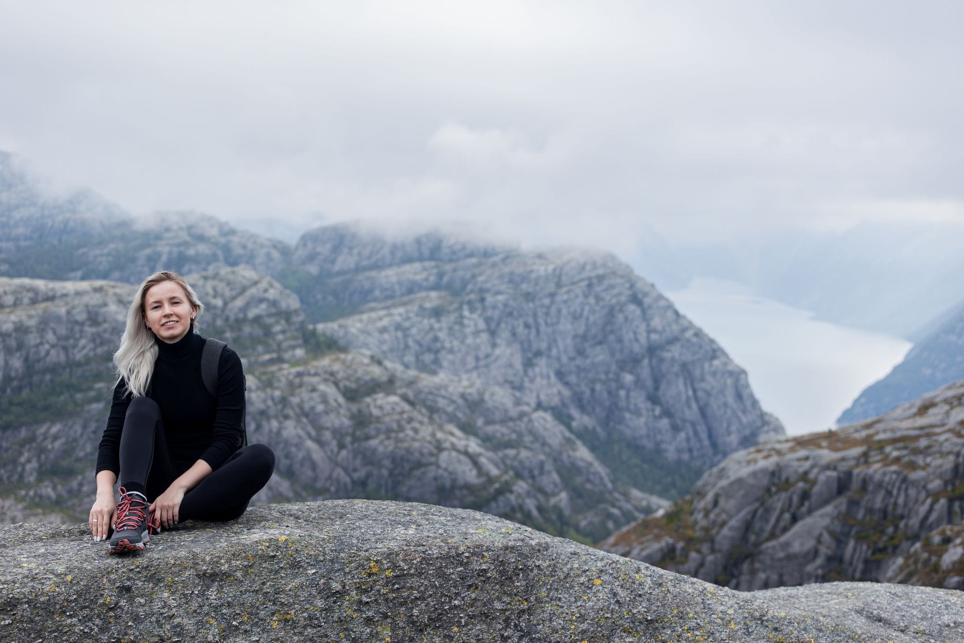 Kobieta siedzi na szczycie góry z widokiem na norweski fiord