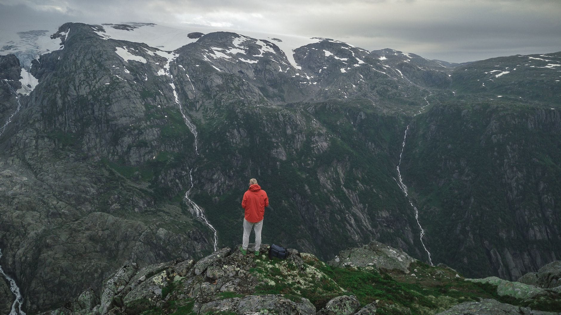 Turysta w czerwonej kurtce na skalistym szczycie w górach Norwegii Turysta w czerwonej kurtce na skalistym szczycie w górach Norwegii
